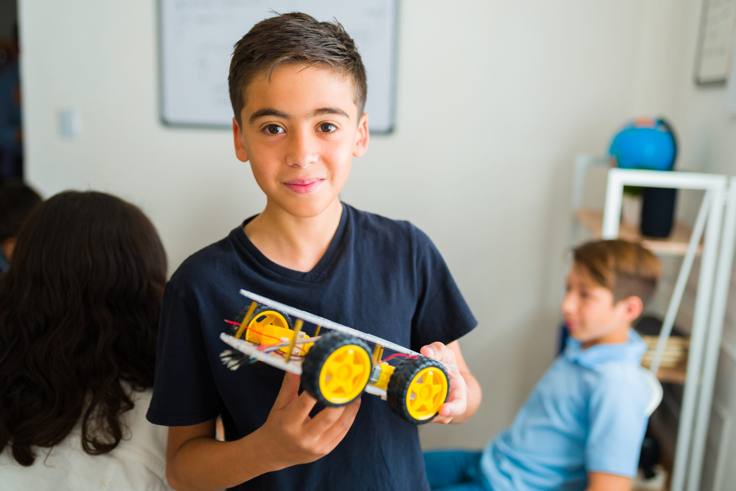 Portrait of a latin young teen boy smiling making eye contact building a robot in his electronics class at junior high school